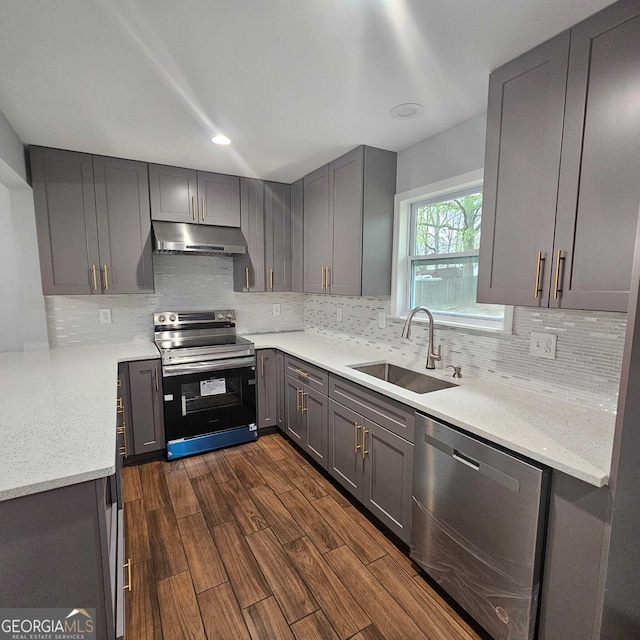 kitchen with dark wood-style floors, under cabinet range hood, a sink, gray cabinetry, and appliances with stainless steel finishes
