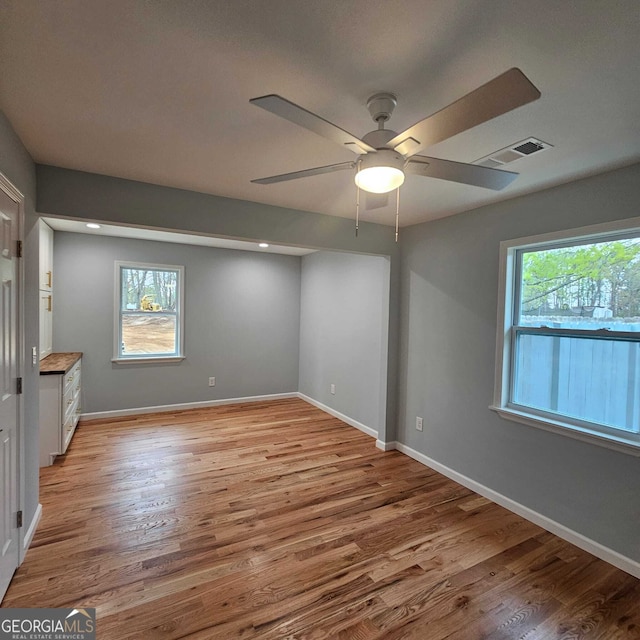 empty room featuring visible vents, light wood-style floors, ceiling fan, and a healthy amount of sunlight