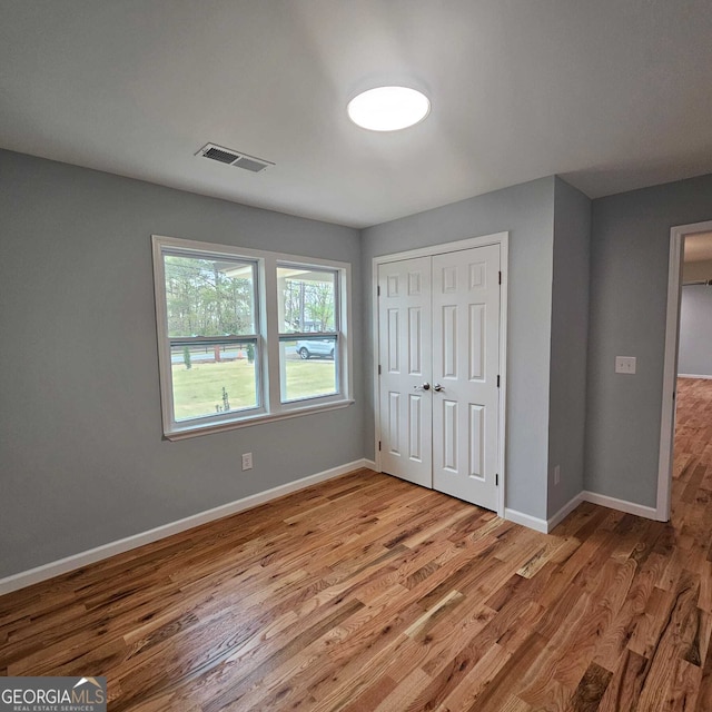 unfurnished bedroom with baseboards, wood finished floors, visible vents, and a closet