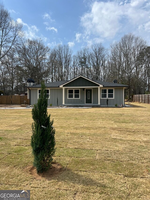back of property with a porch, a chimney, fence, board and batten siding, and a yard