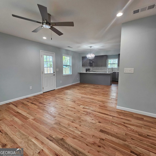 unfurnished living room with ceiling fan with notable chandelier, light wood finished floors, baseboards, visible vents, and recessed lighting