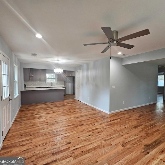 unfurnished living room featuring light wood finished floors, baseboards, visible vents, recessed lighting, and ceiling fan with notable chandelier