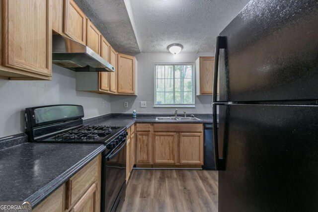 2092 Countydown Ln, Stone Mountain, GA 30088 - kitchen with under cabinet range hood, dark countertops, wood finished floors, a sink, and black appliances