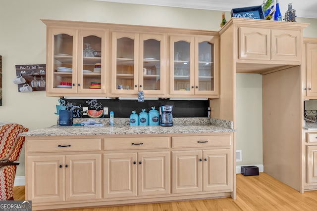 kitchen featuring light wood-type flooring, glass insert cabinets, light brown cabinetry, and light stone countertops