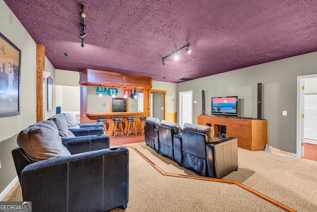 carpeted cinema room with a textured ceiling, baseboards, rail lighting, and visible vents