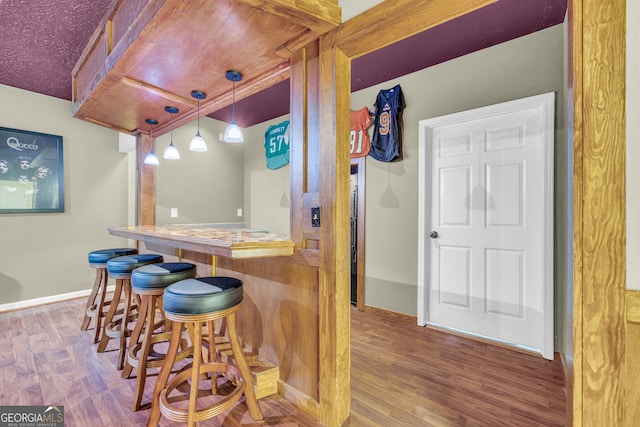bar with a dry bar, wood finished floors, baseboards, and hanging light fixtures