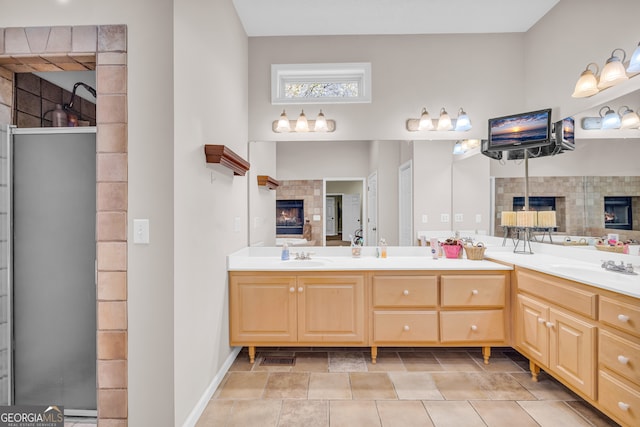 full bath with a warm lit fireplace, stone finish floor, a sink, and double vanity