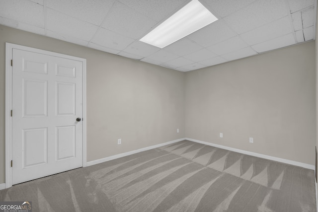 carpeted empty room featuring baseboards and a drop ceiling
