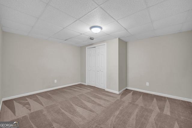 unfurnished bedroom with a closet, baseboards, a drop ceiling, and carpet