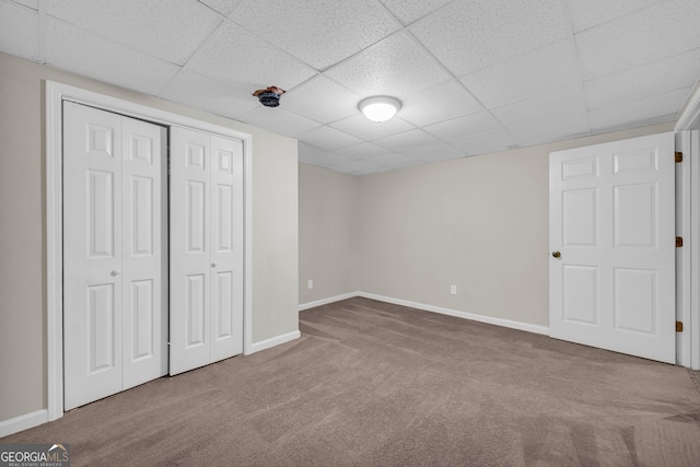 unfurnished bedroom with a closet, a paneled ceiling, baseboards, and carpet floors