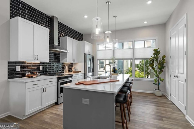 kitchen with a kitchen breakfast bar, light countertops, wall chimney range hood, a sink, and appliances with stainless steel finishes