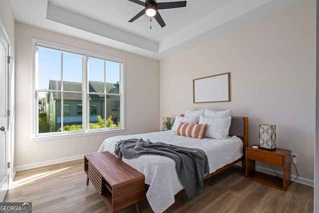 bedroom featuring baseboards, wood finished floors, and a raised ceiling