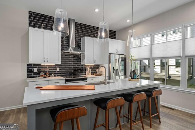 kitchen featuring a sink, stainless steel appliances, wall chimney exhaust hood, baseboards, and visible vents