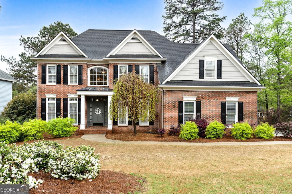 colonial house featuring a front lawn, brick siding, and roof with shingles