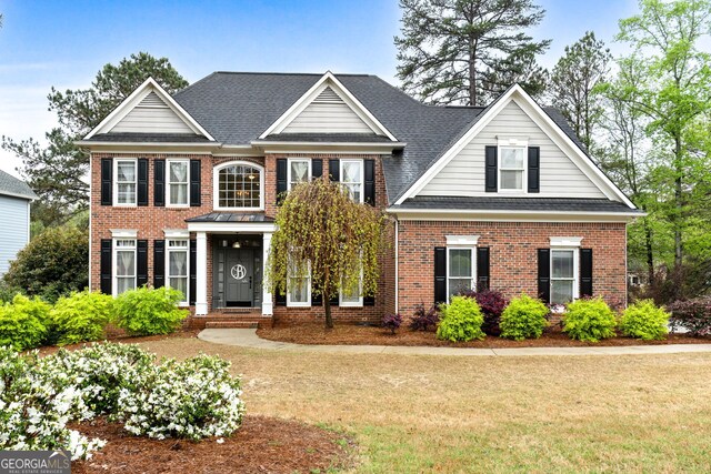 colonial house featuring a front lawn, brick siding, and roof with shingles