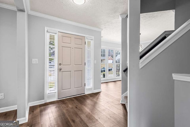 foyer entrance with a textured ceiling, baseboards, stairs, crown molding, and dark wood-type flooring