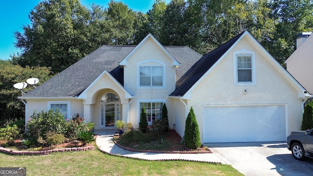 view of front of home featuring an attached garage, driveway, stucco siding, and roof with shingles