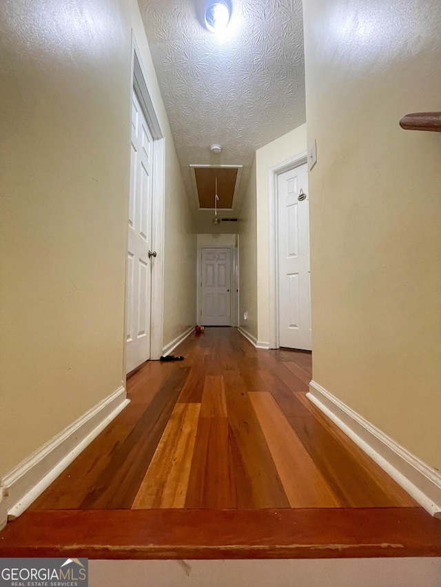 corridor featuring attic access, baseboards, and wood finished floors