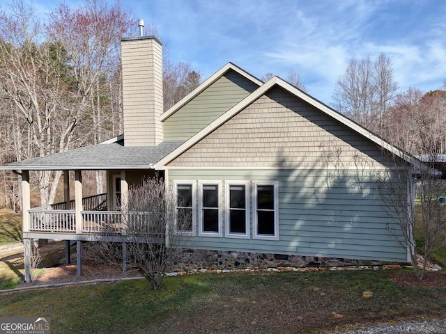 rear view of property with a lawn, a chimney, and roof with shingles