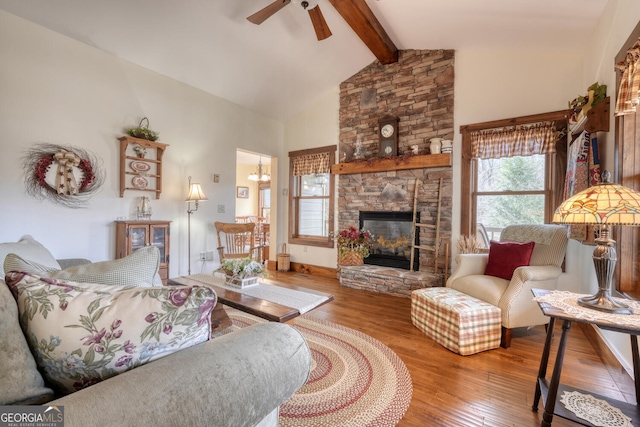 living room featuring lofted ceiling with beams, baseboards, a ceiling fan, wood finished floors, and a stone fireplace