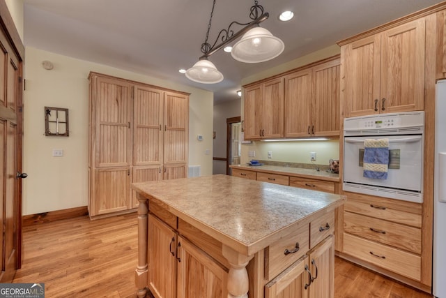 kitchen featuring oven, light countertops, a center island, light wood-style flooring, and hanging light fixtures