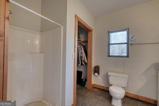 bathroom featuring toilet, tile patterned floors, a stall shower, a walk in closet, and baseboards