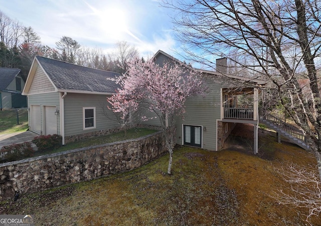 view of home's exterior with a chimney, a garage, a wooden deck, a shingled roof, and stairway