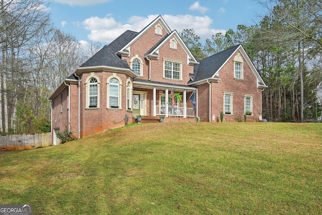 traditional-style house featuring a front lawn, brick siding, fence, and covered porch