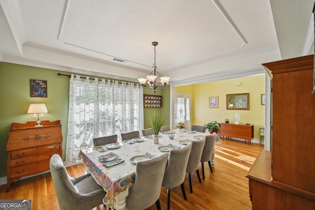 dining room featuring a raised ceiling, visible vents, a chandelier, wood finished floors, and ornamental molding
