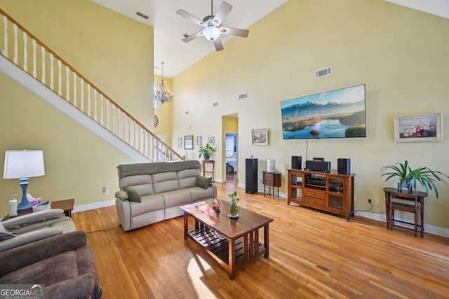 living area featuring high vaulted ceiling, wood finished floors, ceiling fan with notable chandelier, baseboards, and visible vents