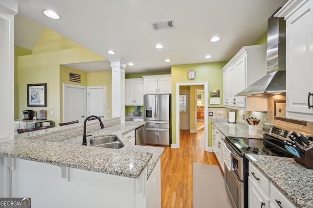 kitchen with wall chimney exhaust hood, stainless steel appliances, a sink, visible vents, and ornate columns