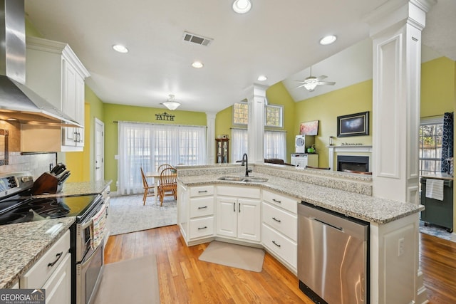 kitchen with a sink, wall chimney exhaust hood, appliances with stainless steel finishes, visible vents, and decorative columns