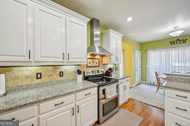 kitchen with backsplash, white cabinets, wall chimney exhaust hood, and double oven range