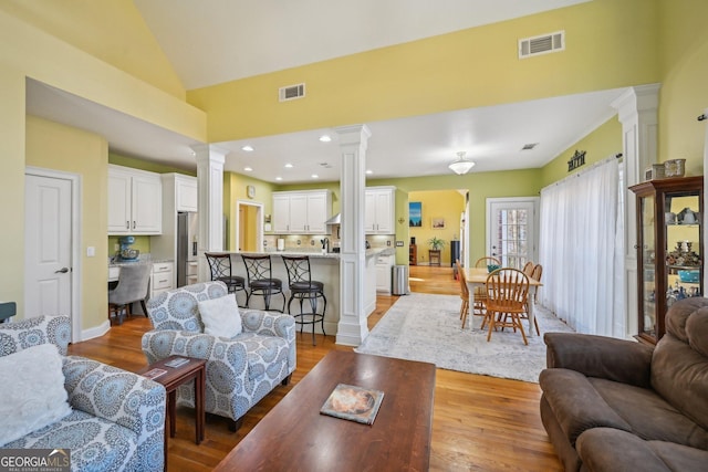 living room featuring light wood finished floors, visible vents, and decorative columns