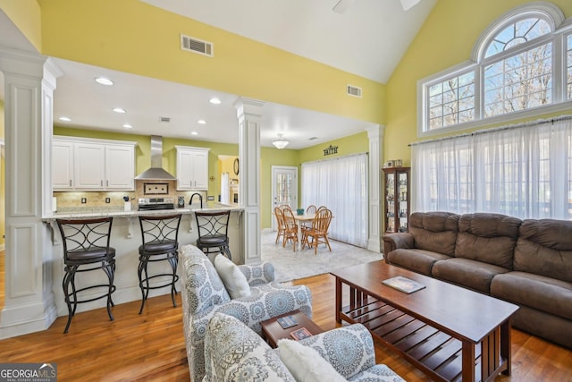 living room with high vaulted ceiling, wood finished floors, decorative columns, visible vents, and recessed lighting