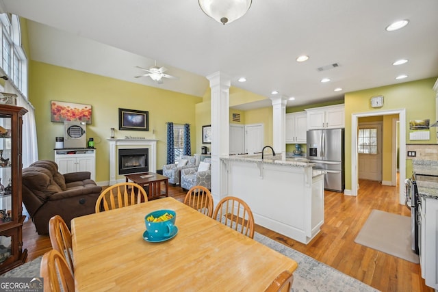 dining space with baseboards, light wood finished floors, visible vents, and decorative columns