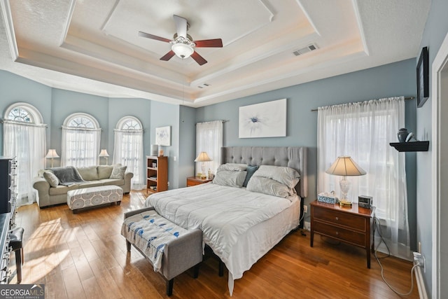 bedroom featuring a ceiling fan, a tray ceiling, visible vents, and hardwood / wood-style floors