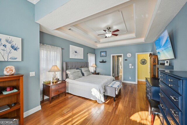 bedroom with baseboards, wood finished floors, a tray ceiling, and visible vents