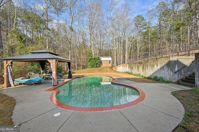 pool with stairs, a patio area, an outdoor structure, a gazebo, and a forest view