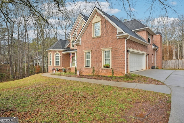 traditional-style house featuring concrete driveway, fence, a front yard, brick siding, and roof with shingles