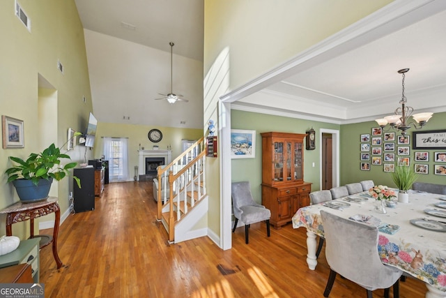 dining space featuring stairway, wood finished floors, visible vents, high vaulted ceiling, and ceiling fan with notable chandelier