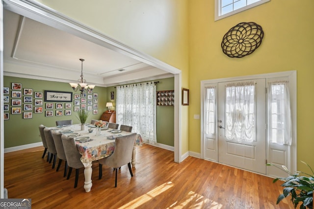 dining area with wood finished floors, a high ceiling, baseboards, and an inviting chandelier