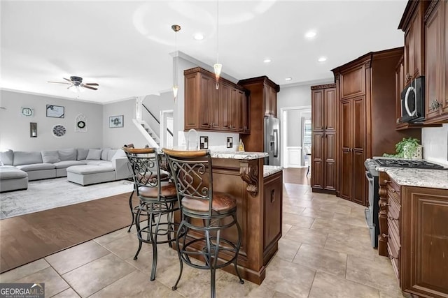 kitchen featuring a ceiling fan, open floor plan, a kitchen bar, a peninsula, and appliances with stainless steel finishes