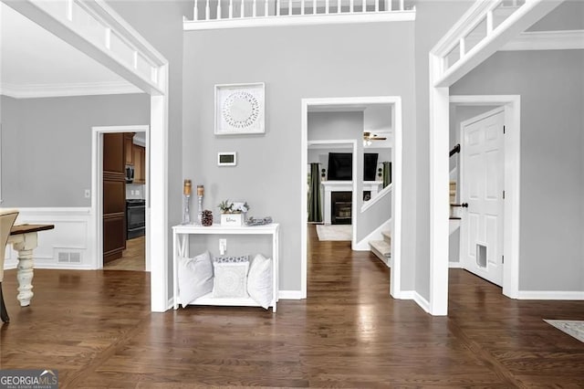foyer entrance with stairway, visible vents, a ceiling fan, crown molding, and a glass covered fireplace