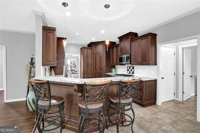 kitchen featuring a breakfast bar area, a peninsula, stainless steel microwave, baseboards, and ornamental molding