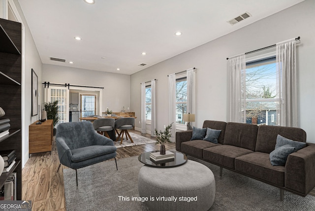 living area with recessed lighting, light wood-type flooring, visible vents, and a barn door