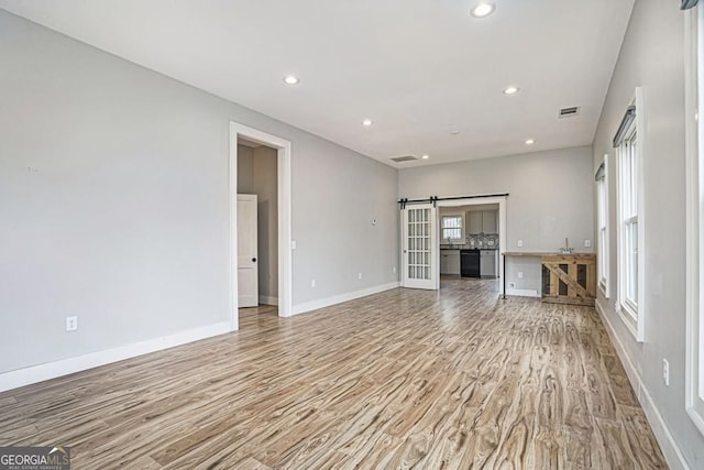 unfurnished living room featuring a barn door, a sink, light wood-style floors, baseboards, and recessed lighting