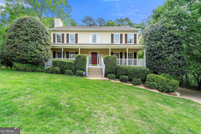 colonial-style house with a chimney, a porch, and a front yard