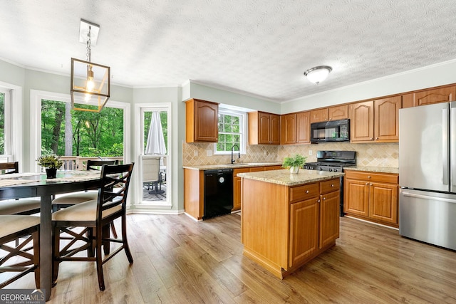 kitchen with a sink, light wood finished floors, a center island, decorative backsplash, and black appliances