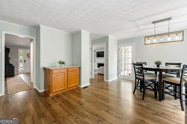 dining space with a fireplace, ornamental molding, baseboards, visible vents, and dark wood-style floors